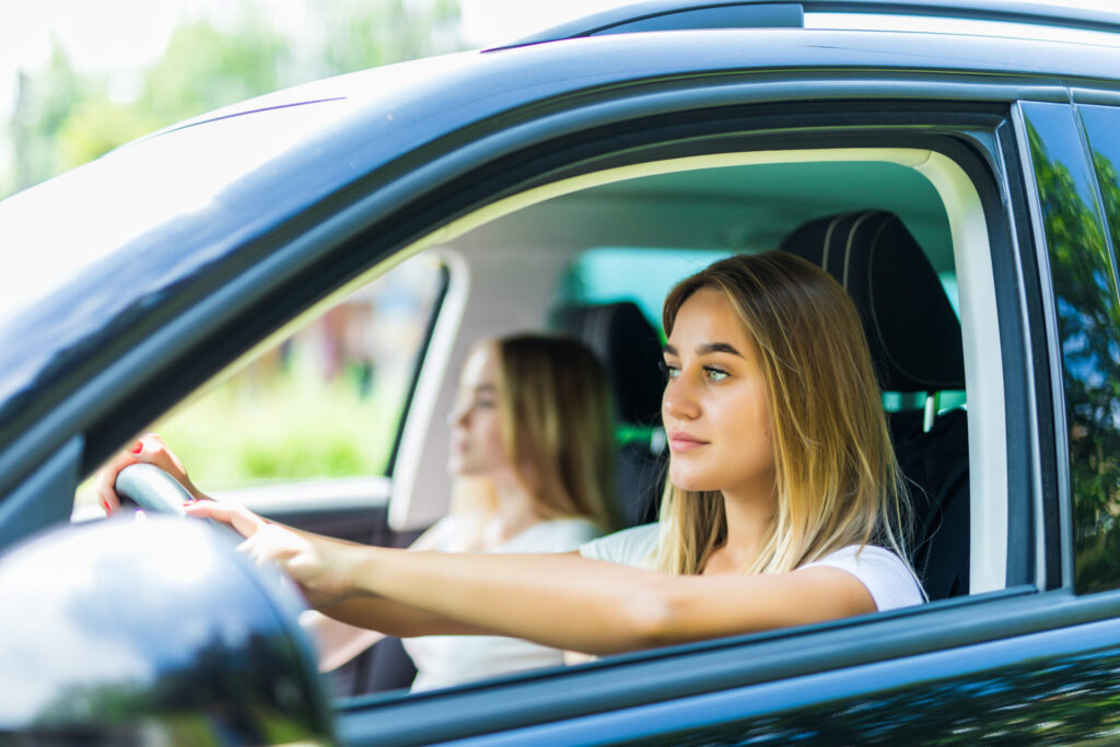 Two cheerful young women smiling while sitting in a car, embodying the spirit of freedom and new driving laws for teens.