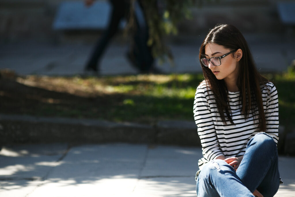 A fashionable model wearing glasses sits thoughtfully, representing the warning signs of mental illness in teens.