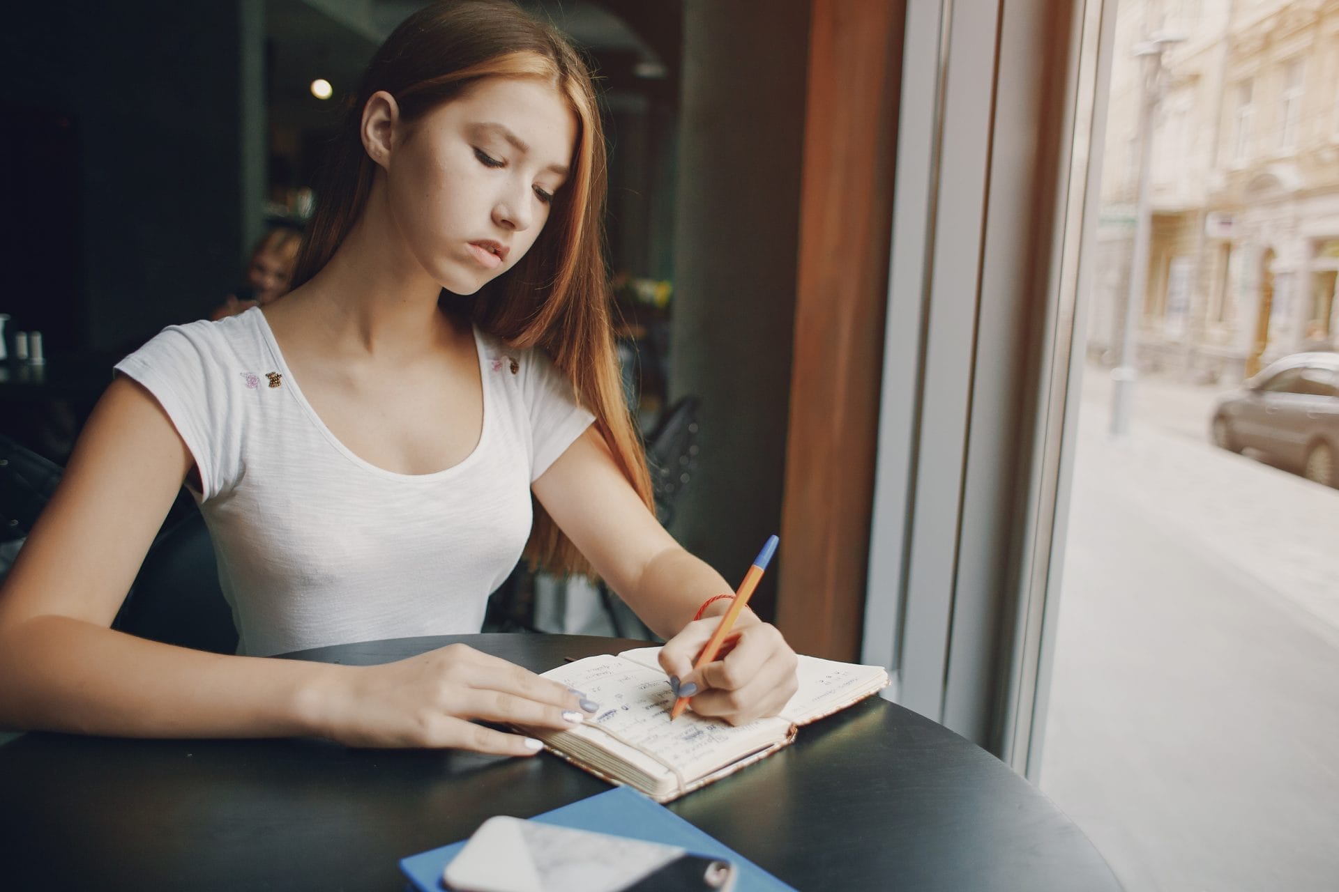 Teenage girl sitting at the table at a café and writing in her journal