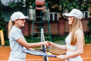 Happy girls playing tennis, shaking hands and smiling, enjoying recreational activities for teens that build skills.