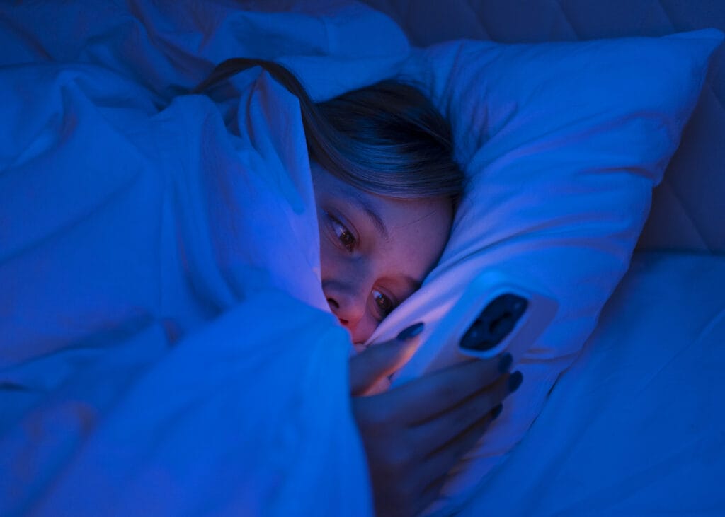 Teen under the covers using a phone late at night