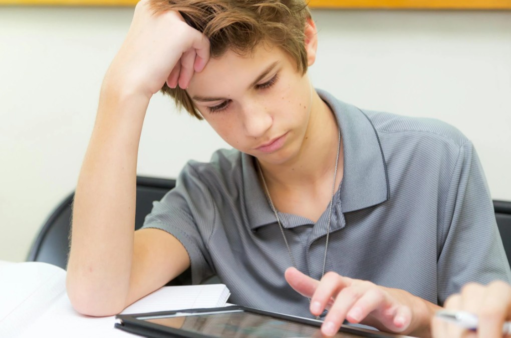 financial emergencies impact on teen decisions - A teenage boy sitting at a desk with a laptop, contemplating financial decis