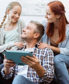 safe programs for troubled teens - Smiling parents and a teenage girl using a digital tablet together at home, showcasing fam