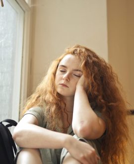 A teenage girl sitting on a bed, looking worried while holding her head, illustrating how to identify teen anxiety symptoms.