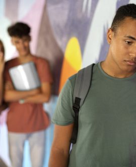 A distressed teenager sitting alone on a school bench, reflecting on common causes of teen behavioral problems like bullying.