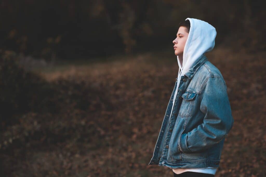 Best Wilderness Therapy for Teens 1 handsome teen boy wearing denim jacket and white hoodie standing outdoors over nature autumn